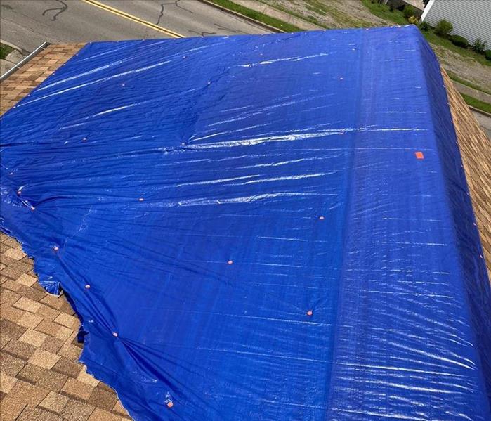 The damaged roof is covered with a blue tarp.