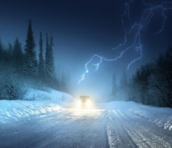 image of a car driving during an extreme thundersnow storm with lightning in the backdrop