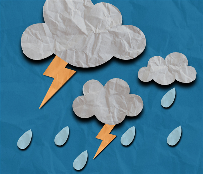 Paper cut outs of clouds, lightning, and rain sit on a blue paper.